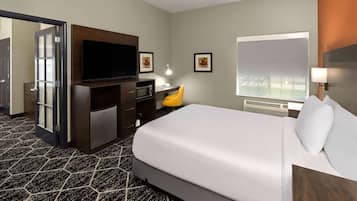 Una habitación de hotel con una cama grande, un escritorio con televisión de pantalla plana, una lámpara de escritorio, una silla, un microondas y un ventanal amplio.