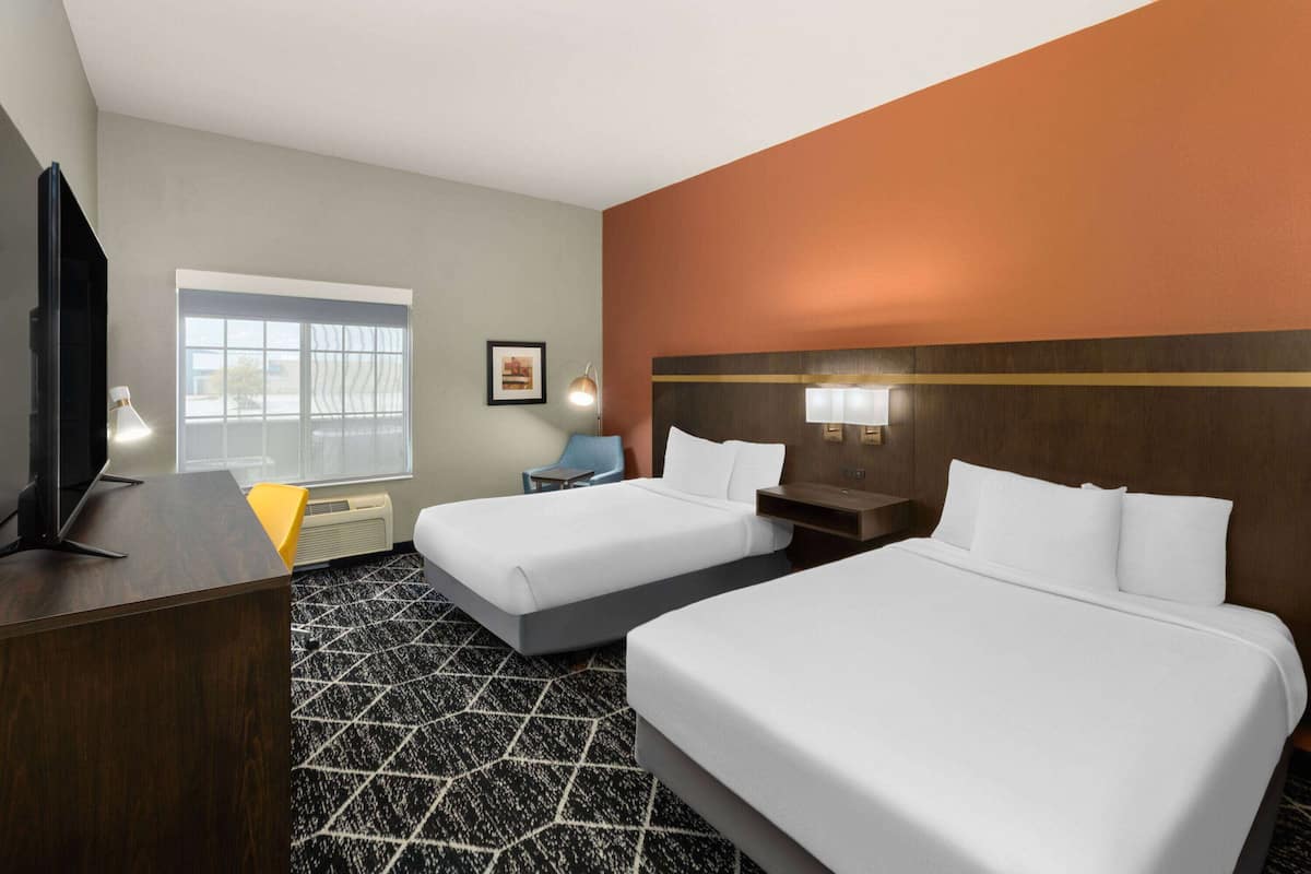 A hotel room with two beds, a desk, a chair, a TV, and a window.