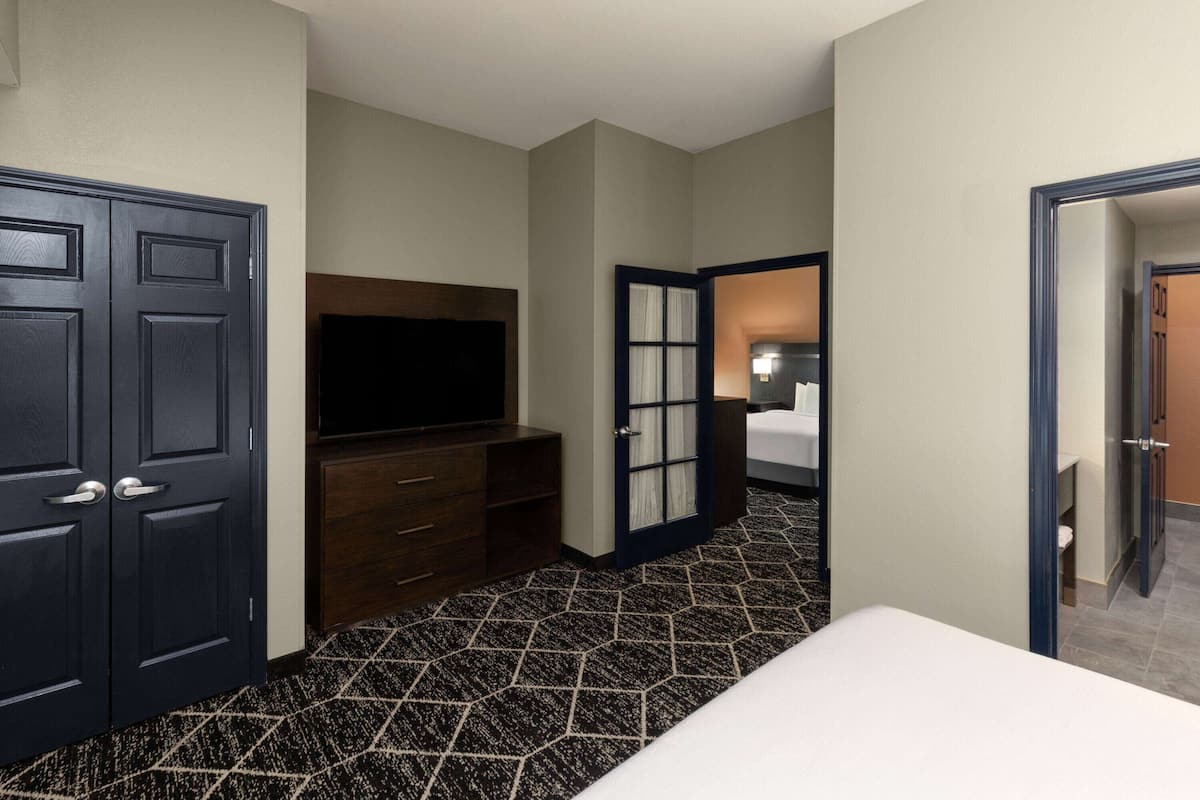 A hotel room with a large bed, a TV, a dresser, and a door leading to another room.