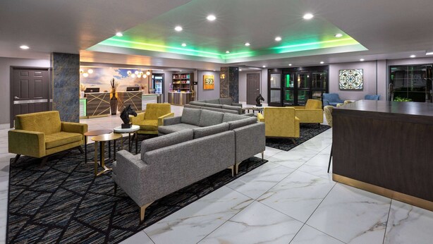 A modern lobby with a reception desk, seating area, and a bar. - La Quinta Inn & Suites by Wyndham Olathe (Olathe)