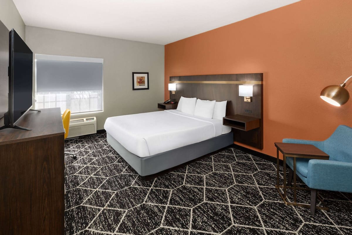 A hotel room with a large bed, a desk, a chair, a TV, and a window.