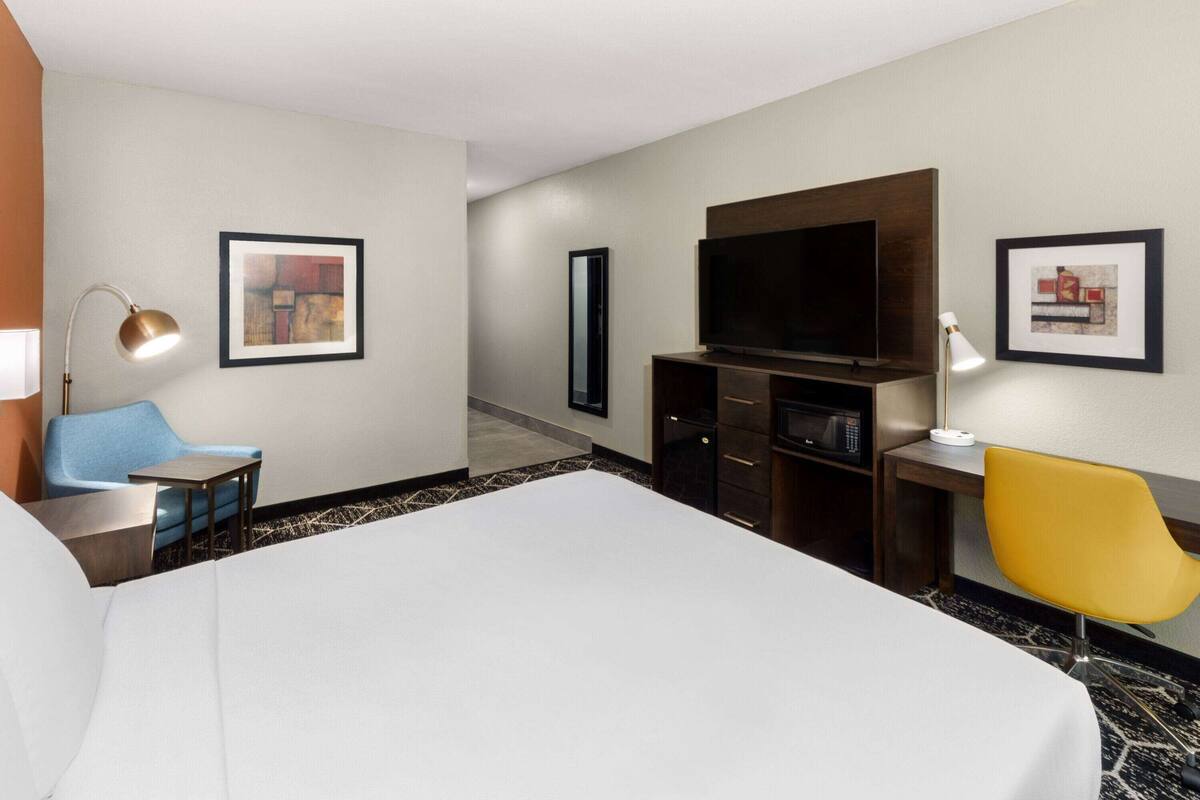 A hotel room with a large bed, a desk with a chair, a flat-screen TV, a microwave, and artwork on the walls.