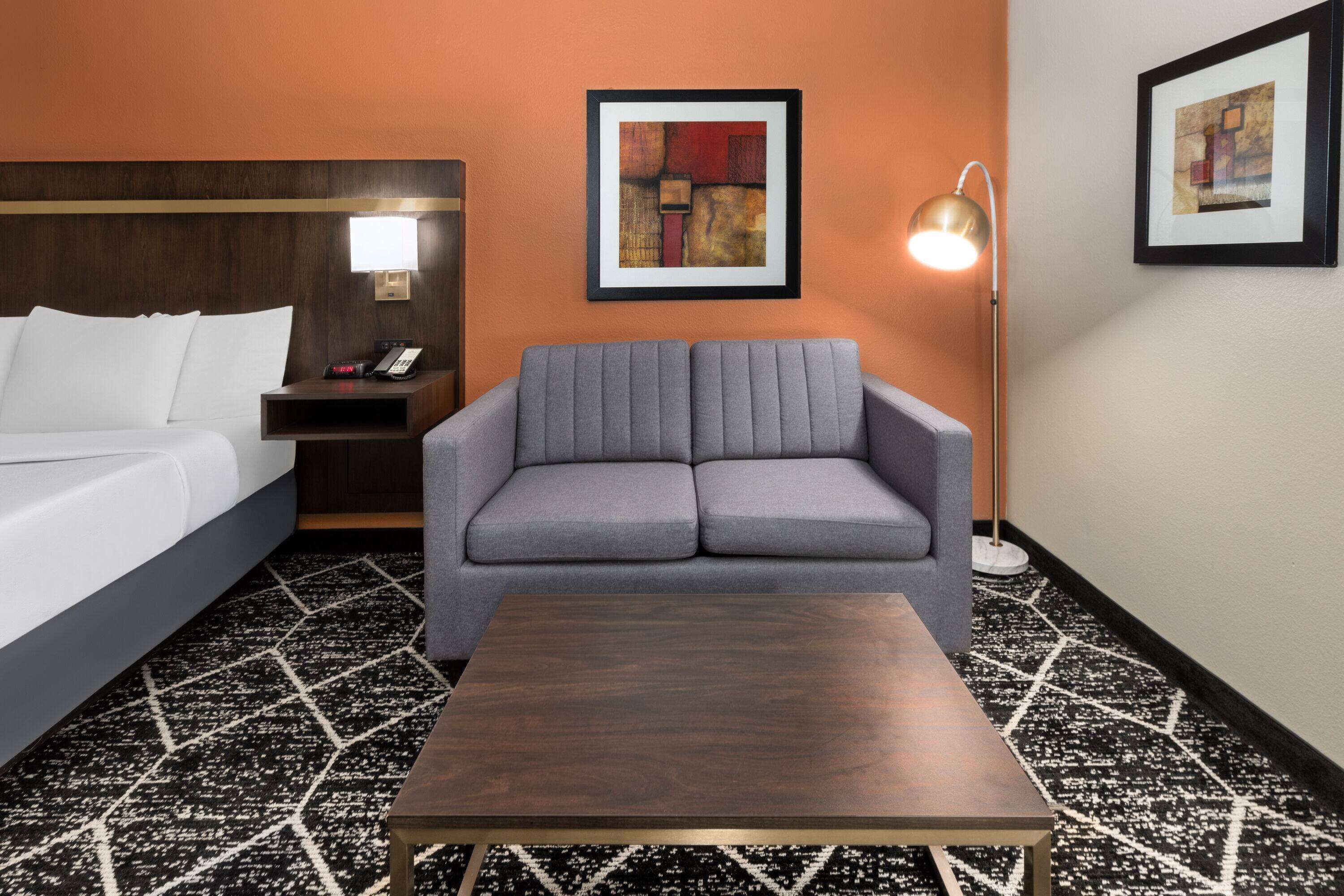 Une chambre d’hôtel avec un lit, un canapé gris, une petite table et deux œuvres d’art encadrées accrochées aux murs.