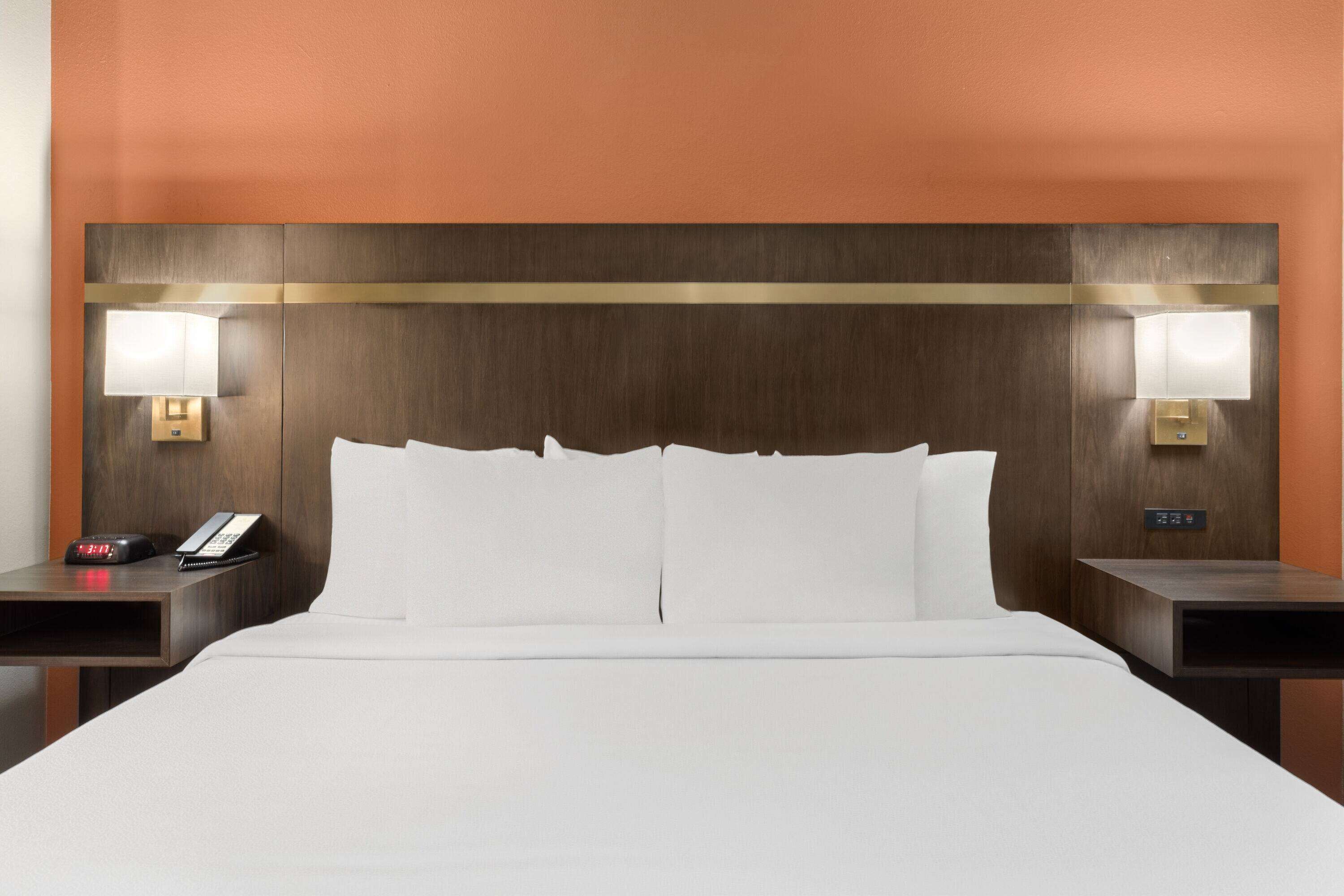 A hotel room with a large bed, two bedside tables, a nightstand, a wall-mounted lamp, and a phone on the nightstand.