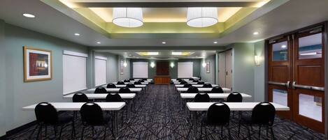 A conference room with rows of tables and chairs, a patterned carpet, and ceiling lights.