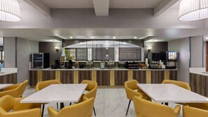 A modern restaurant with a bar area, yellow chairs, and a counter with a TV and vending machines. - La Quinta Inn & Suites by Wyndham Olathe (Olathe)