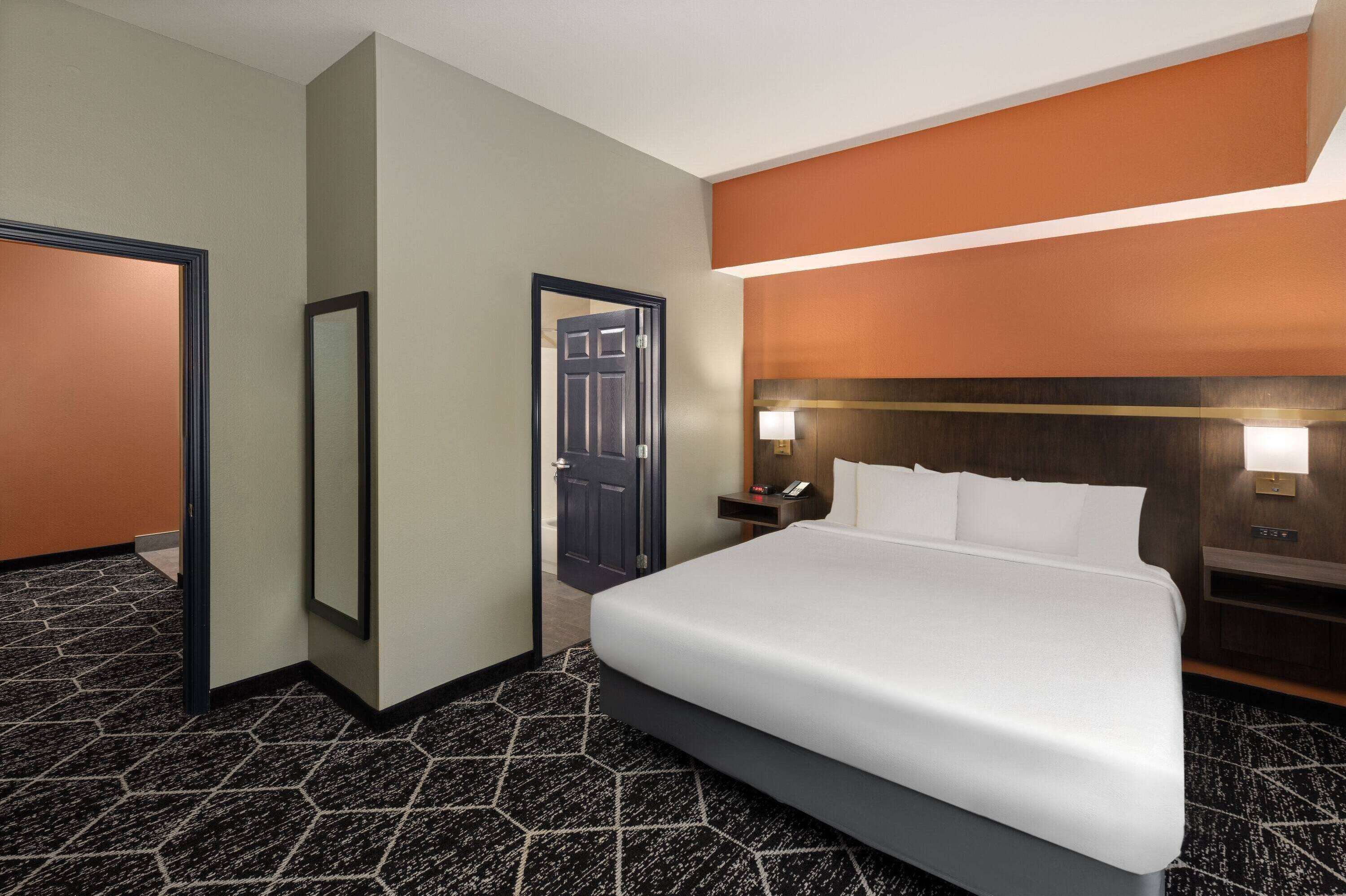 Une chambre d’hôtel avec un grand lit, une table de chevet avec une lampe, une porte et un miroir.