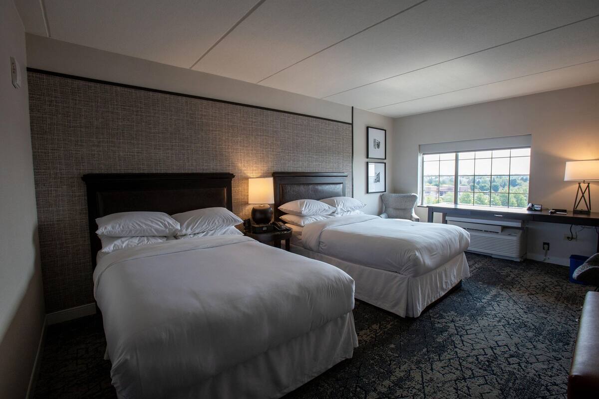 Une chambre d’hôtel avec deux lits, un bureau, une chaise et une fenêtre donnant sur un paysage agréable.