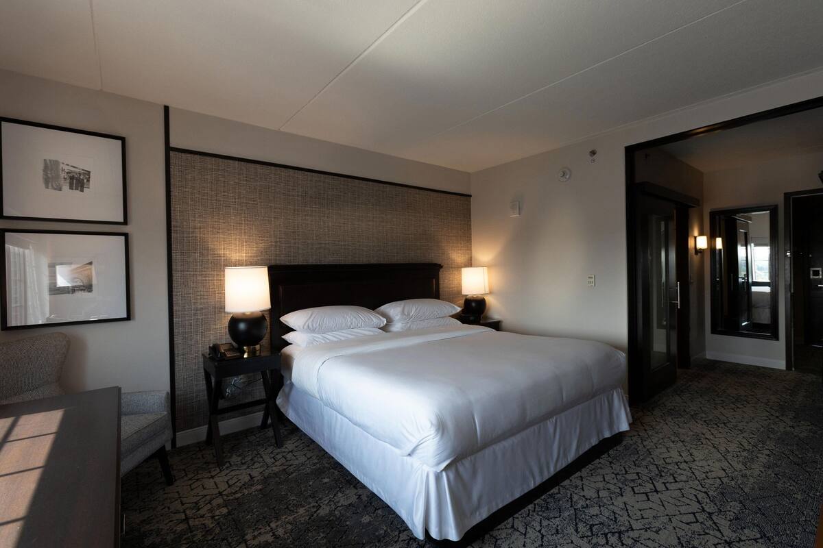 Une chambre d’hôtel avec un grand lit, deux tables de chevet avec des lampes, une chaise et des tableaux encadrés au mur.