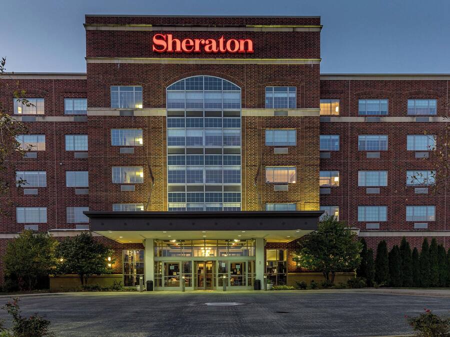 A Sheraton hotel with a brick facade, large arched windows, and a well-lit entrance.