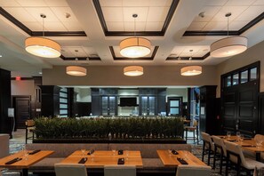 A modern hotel lobby with a central seating area, multiple dining tables, and a decorative plant wall. - Sheraton Chicago Northbrook Hotel (Northbrook)