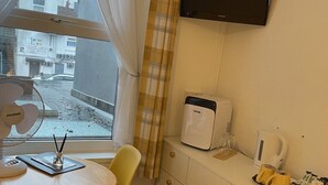 A small room with a window, a table with a chair, a TV, a microwave, and a coffee maker.