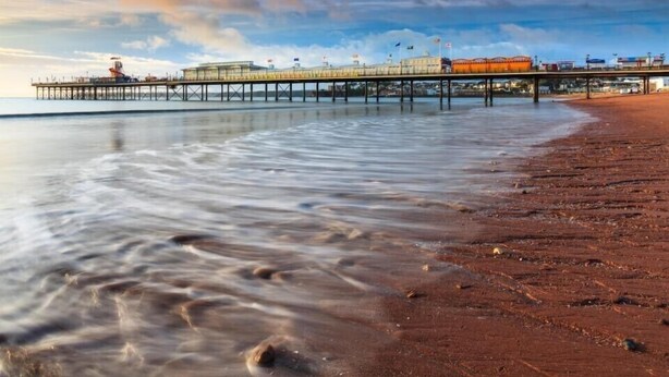 A pier extending into calm waters with a sandy beach on the right.