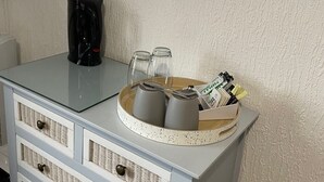 A white dresser with a round mirror, a coffee maker, and a tray with cups and a basket of items.