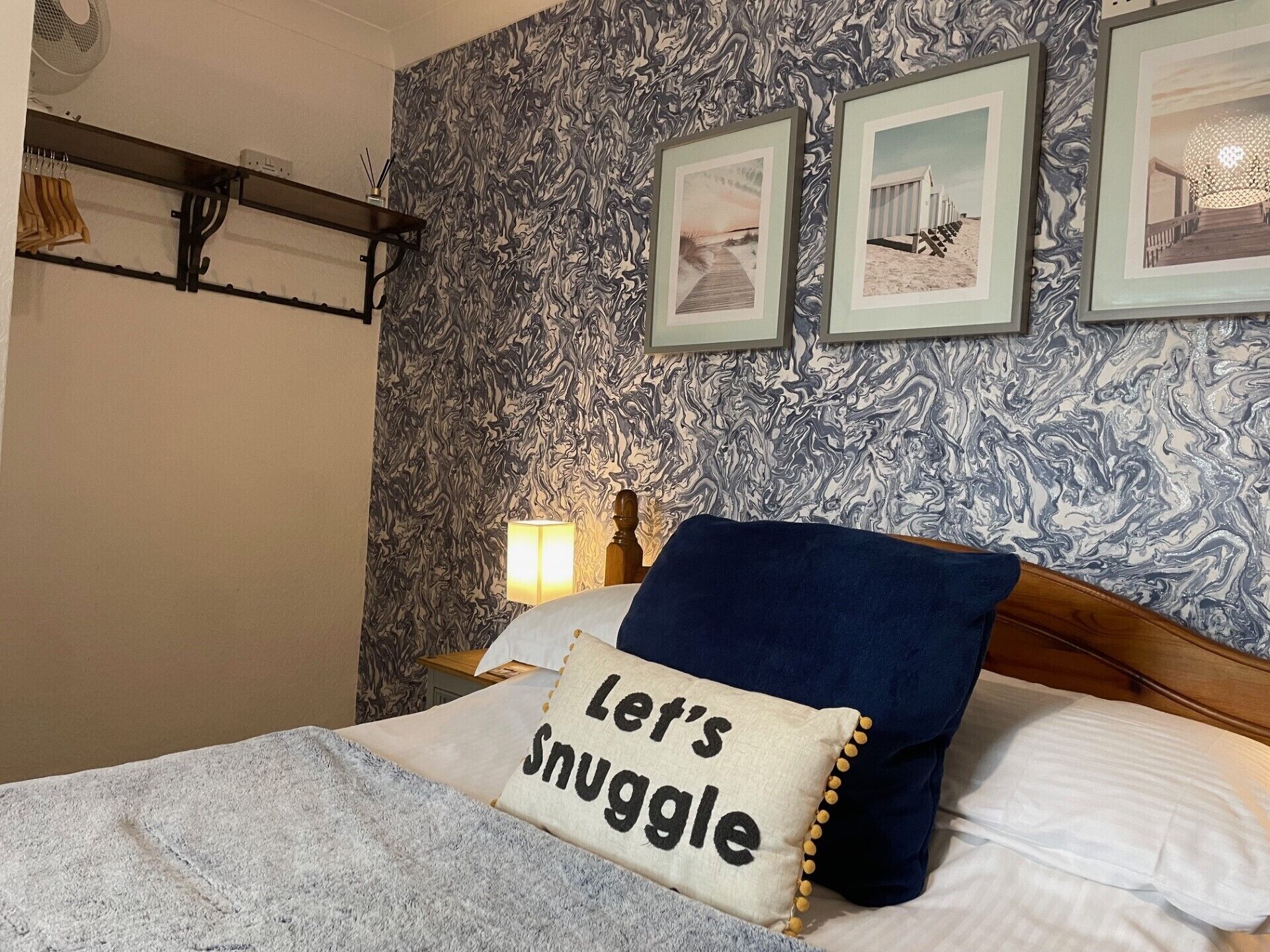 A bedroom with a bed, a wall with a marbled pattern, and three framed pictures on the wall.