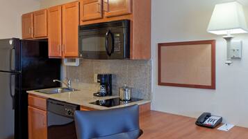 A compact hotel kitchen with wooden cabinets, a stainless steel refrigerator, a microwave, a coffee maker, and a telephone.