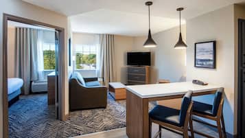 A hotel room with a bed, a sofa, a TV, a desk with chairs, and a view of the outdoors.