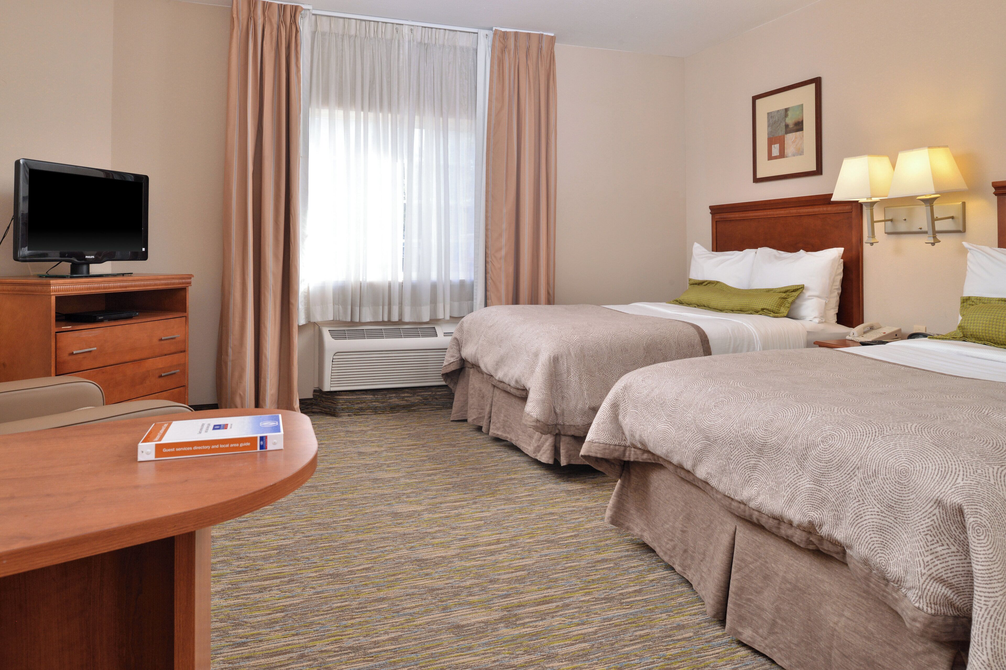 A hotel room with two beds, a desk with a television, a chair, and a lamp.