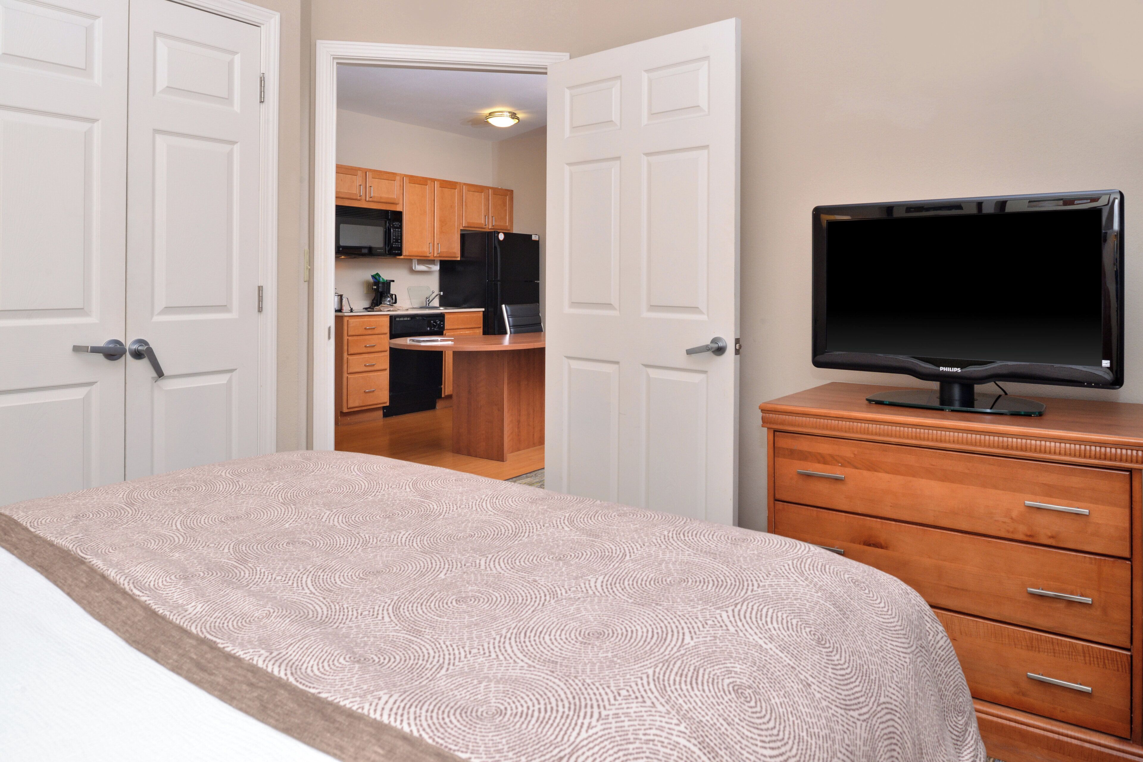 Una habitación de hotel con una cama, un televisor sobre un aparador de madera y vistas al área de la cocina.