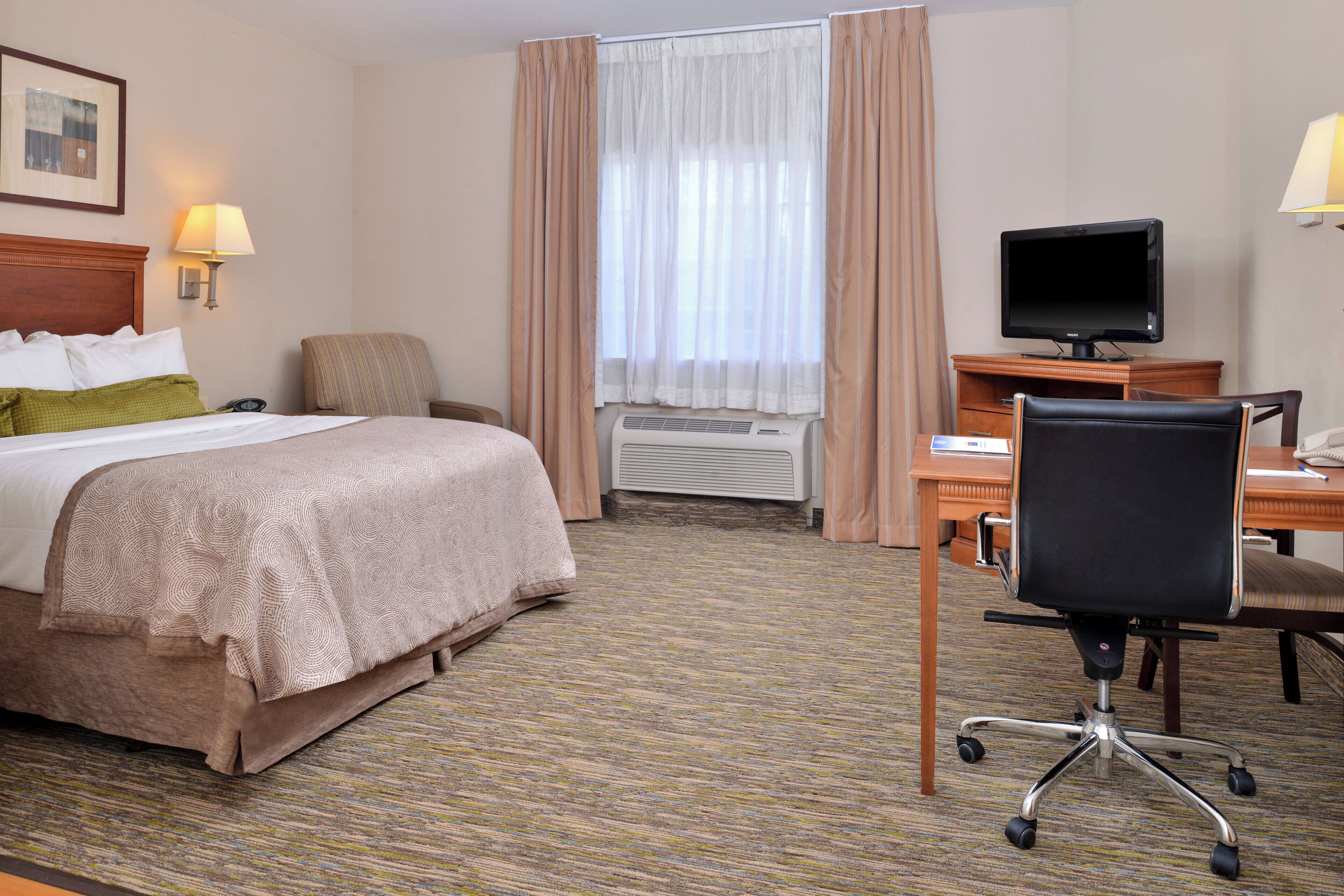 A hotel room with a bed, a desk, a chair, a television, and a window with curtains.