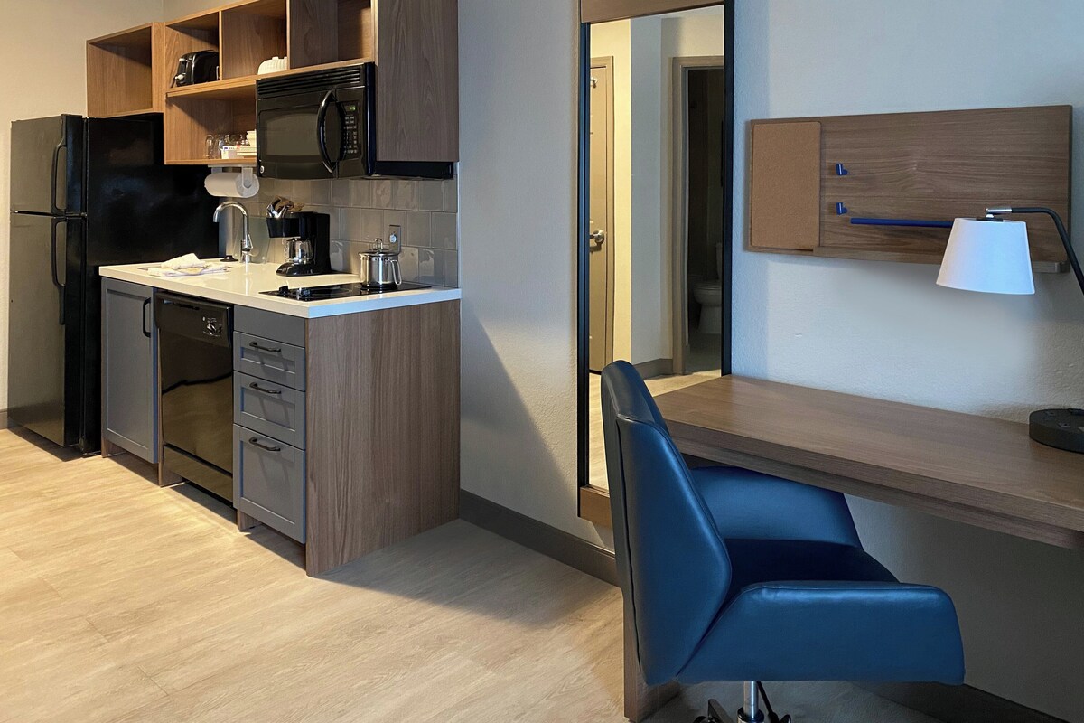 A modern kitchen with a built-in microwave, refrigerator, and dishwasher. There is a wooden countertop and a blue chair.