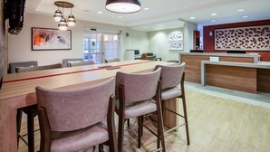 Un comedor moderno con una larga mesa de madera, tres taburetes de bar e iluminación colgante.