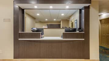 A reception desk with two counters, a wall-mounted phone, and a sign indicating front desk hours.