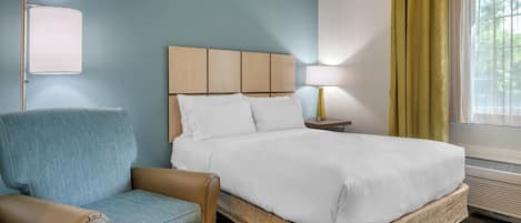 A hotel room with a bed, a chair, a nightstand, and a window with curtains.
