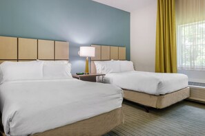 Une chambre d’hôtel avec deux lits, une table de chevet, une lampe et une fenêtre avec des rideaux.