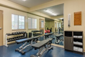 Een sportschool met trainingsapparatuur, banken, gewichten en een spiegel.