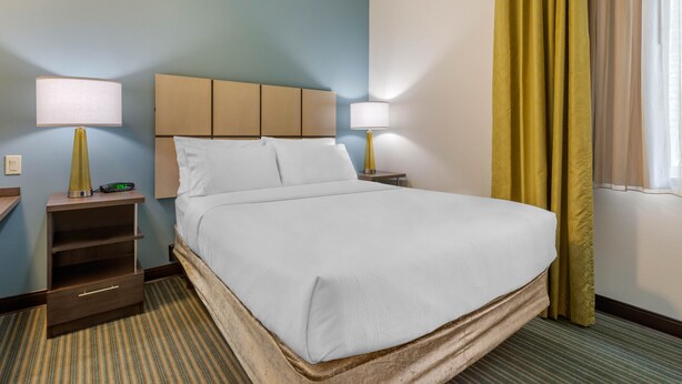 A hotel room with a large bed, two bedside tables with lamps, a nightstand, and a window with curtains. - Candlewood Suites Fort Myers Sanibel Gateway by IHG (Fort Myers)