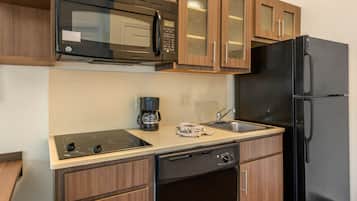 Una cocina compacta con microondas, cafetera, lavabo, lavavajillas y un refrigerador negro.
