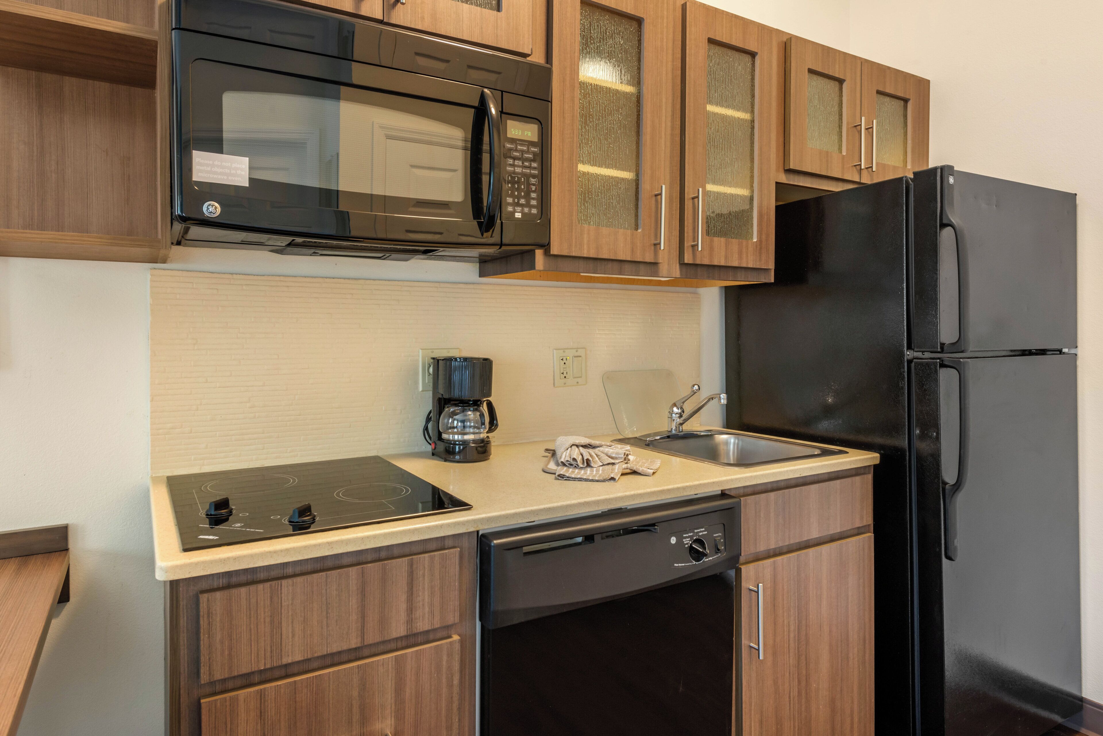 A compact kitchen with a microwave, coffee maker, sink, and a black refrigerator.