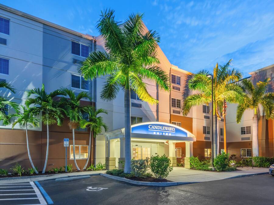 A hotel entrance with a sign reading 'Candlewood Suites' and a parking lot with a handicapped parking space.