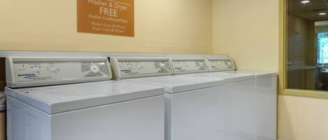 A row of white commercial heavy-duty washers and dryers with a sign above stating they are free to use.