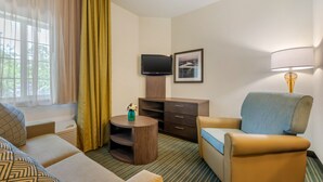A hotel room with a sofa, armchair, TV, and a small table with a vase. - Candlewood Suites Fort Myers Sanibel Gateway by IHG (Fort Myers)