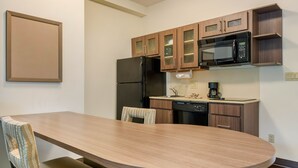 A compact kitchen with a wooden table, chairs, a refrigerator, a microwave, and cabinets. - Candlewood Suites Fort Myers Sanibel Gateway by IHG (Fort Myers)