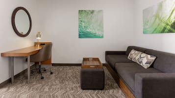 Een moderne kamer met een bureau, stoel, bank, voetenbankje en kunstwerken aan de wanden.