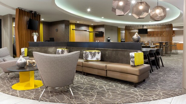 Un hall d’hôtel moderne doté d’un comptoir d’accueil incurvé, d’un espace salon avec des canapés et des fauteuils, et d’un espace repas avec des tables et des chaises.