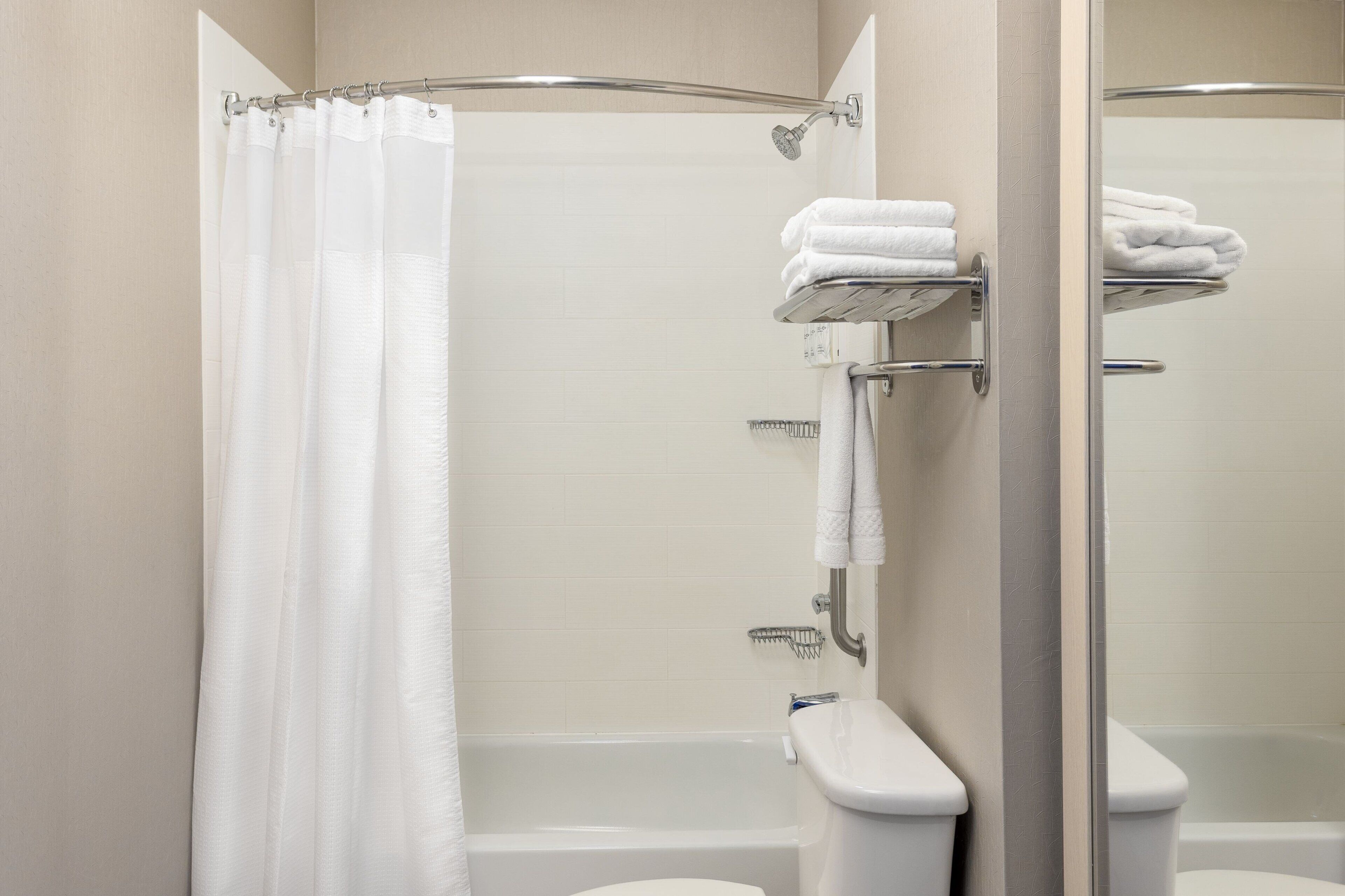 A bathroom with a shower curtain, a toilet, and a towel rack with folded towels.
