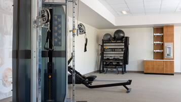 A gym with exercise equipment, a wall-mounted rack with weights, and a water dispenser.