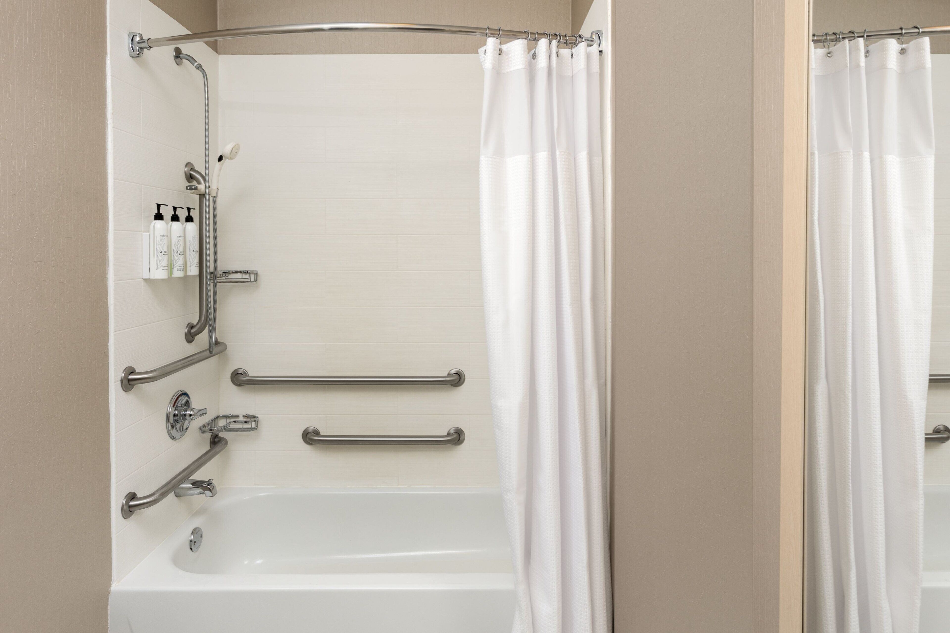 Un baño con una bañera blanca, barras de apoyo y una cortina de ducha.