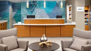 Un espace d’accueil au design moderne, comprenant un comptoir de réception, deux fauteuils, une table ronde agrémentée d’un vase décoratif et un mur orné d’un motif géométrique.