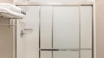Una doccia con porta in vetro, un portasacchiuni con asciugamani piegati e articoli da toilette a parete.