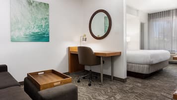 A hotel room with a desk, chair, bed, and a small wooden side table.