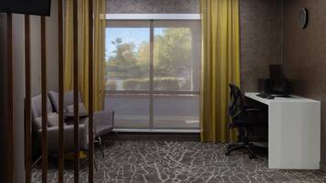 Quarto de hotel com uma escrivaninha, uma cadeira, uma janela grande com cortinas amarelas e vista para o exterior.