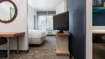 A hotel room with a bed, a desk, a television, and a large window with curtains.