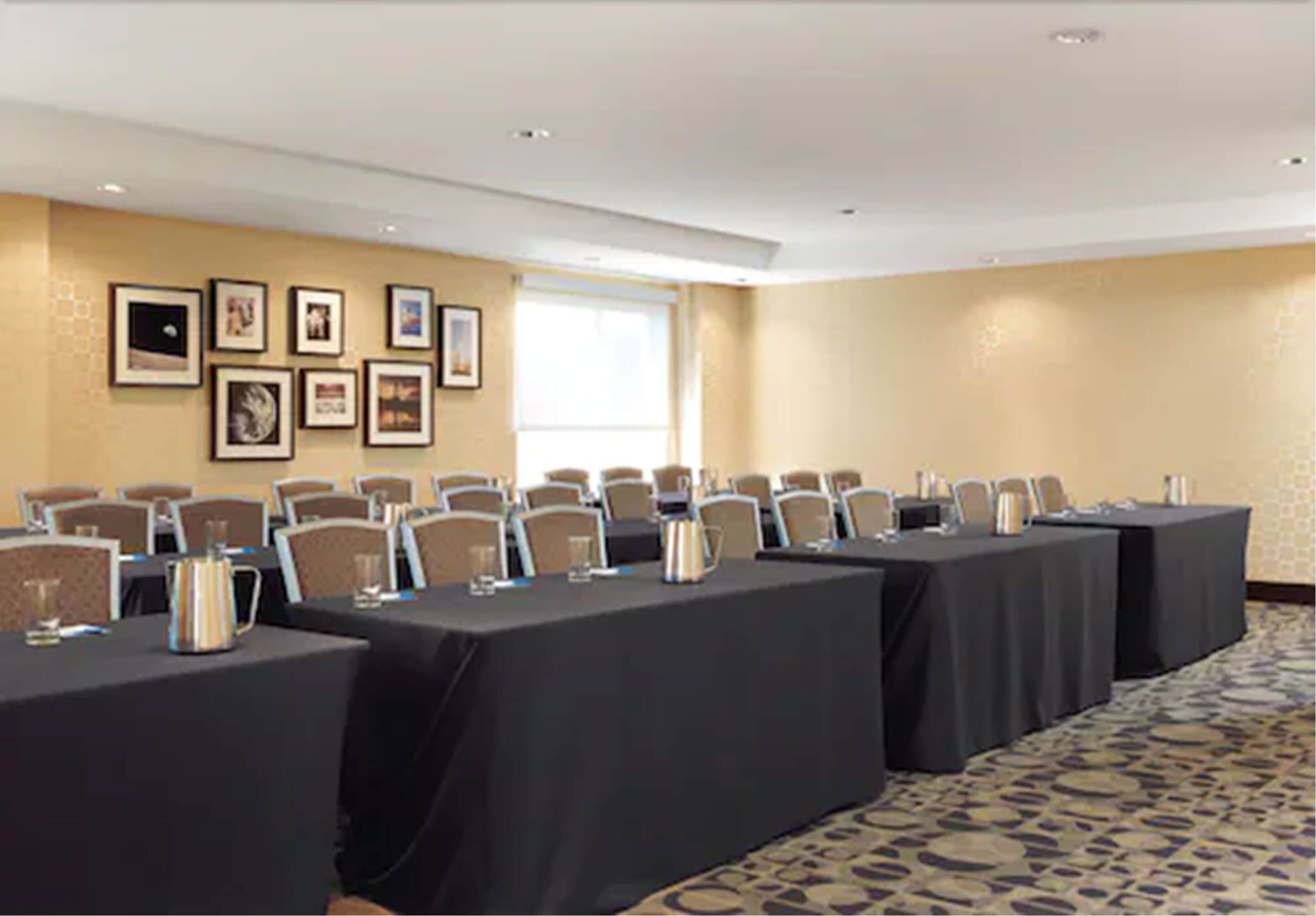 Uma sala de conferências com mesas compridas, cadeiras e quadros nas paredes.