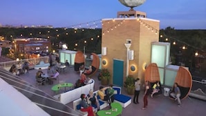 Una terraza en la azotea con zonas de estar, una escultura decorativa de luna y luces colgantes.
