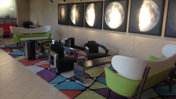 Un hall d’entrée au design moderne, comprenant un espace salon avec des fauteuils et un canapé aux couleurs vives, une table basse et un mur orné de photographies de la lune encadrées.
